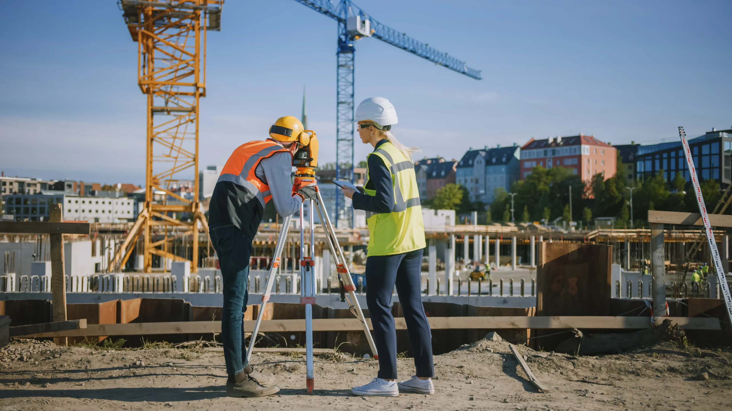 A construction worker looking through a three-legged camera
